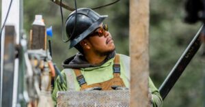 Construction worker in a hard hat and safety glasses looks up at a task on a construction site.